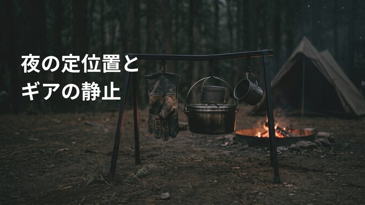 キャンプサイトの地面に自立し、クッカーや食器が吊り下げられた黒いアルミ製のハンガーラック。