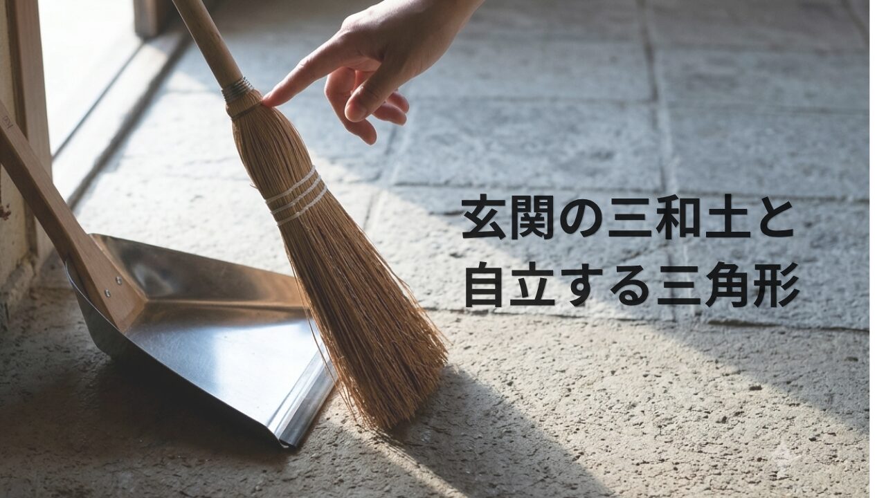 玄関の隅に自立している、銀色の金属製ちりとりと木製ハンドルの箒。