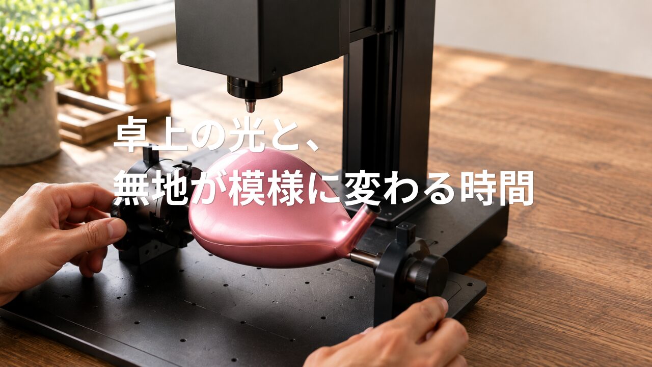 卓上レーザー彫刻機のロータリーアタッチメントに固定された、彫刻前の無地の金属製ゴルフクラブヘッド。